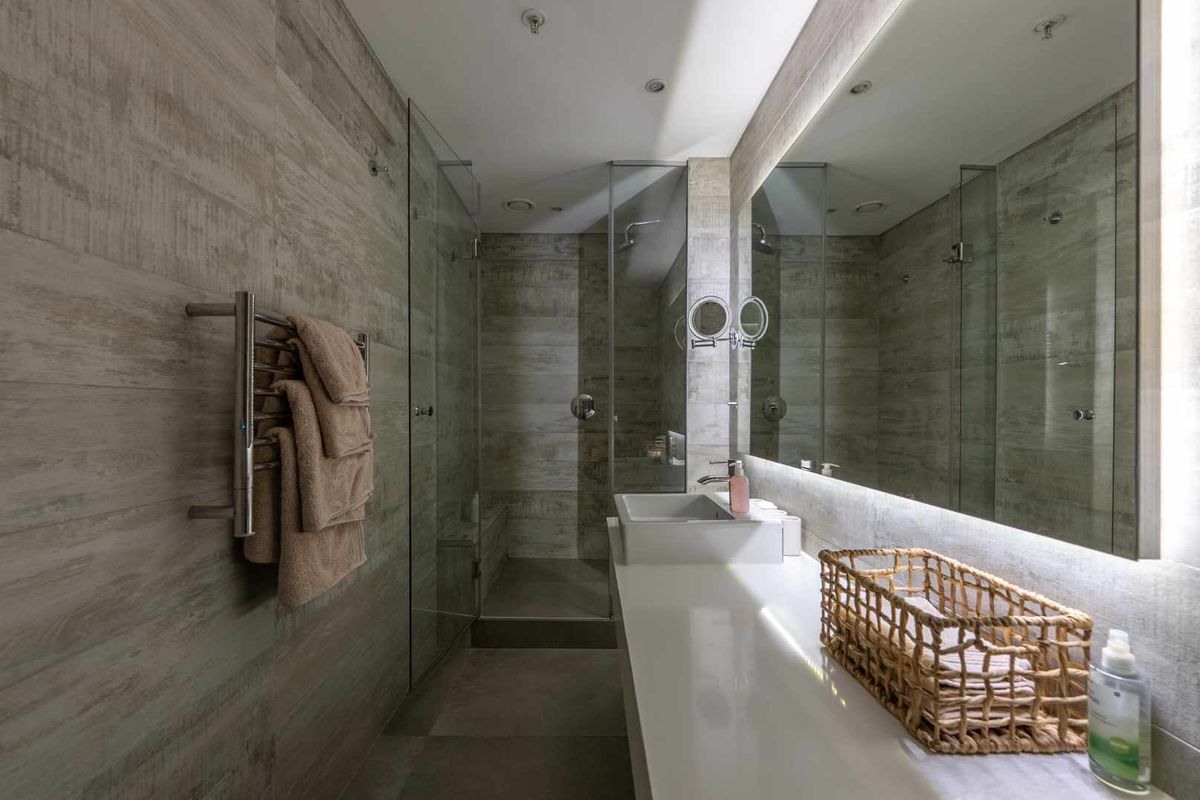 Modern bathroom featuring a walk-in glass shower, wall-mounted heated towel rail, large vanity mirror, and contemporary basin with integrated lighting.