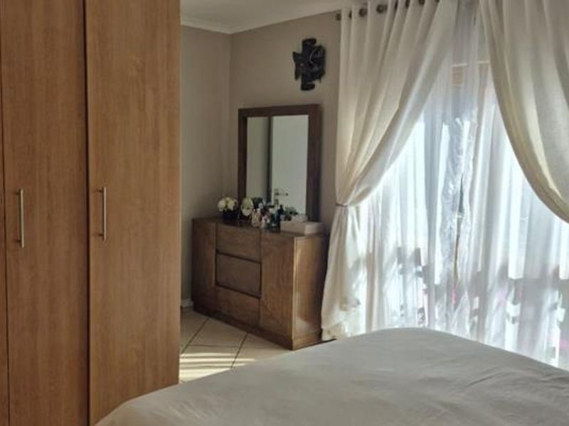 A well-maintained bedroom featuring built-in wooden cupboards, tiled flooring, and large windows with curtains allowing for natural light.