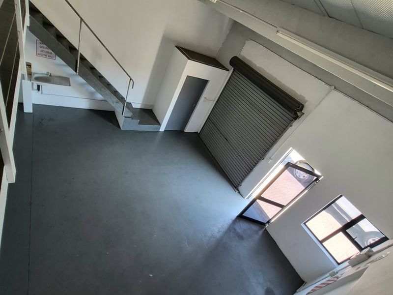 Spacious industrial utility area featuring a roller shutter door, metal staircase, and exposed ceiling beams, suitable for workshop or storage use.