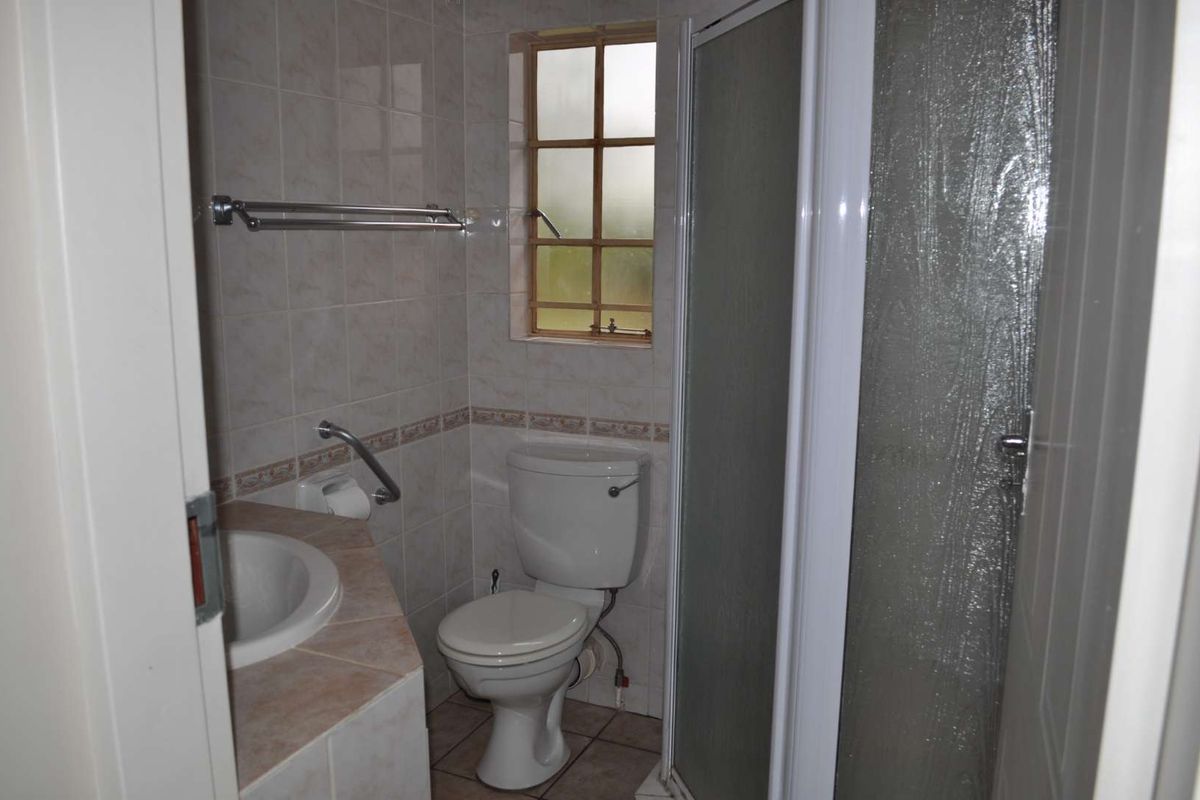 A functional bathroom featuring a corner vanity, toilet, and a glass-enclosed shower with tiled walls and flooring.