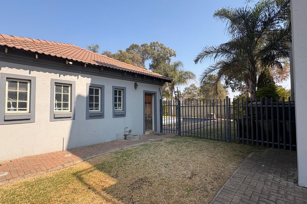 Rear exterior view of the property featuring a paved walkway, lawn area, and steel security fencing enclosing the garden space.