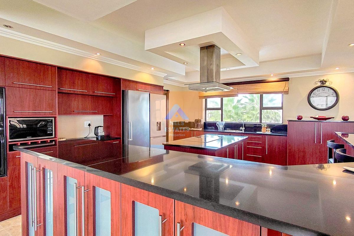 Spacious kitchen featuring dark wood cabinetry, black granite countertops, a central island, and a stainless steel extractor fan.