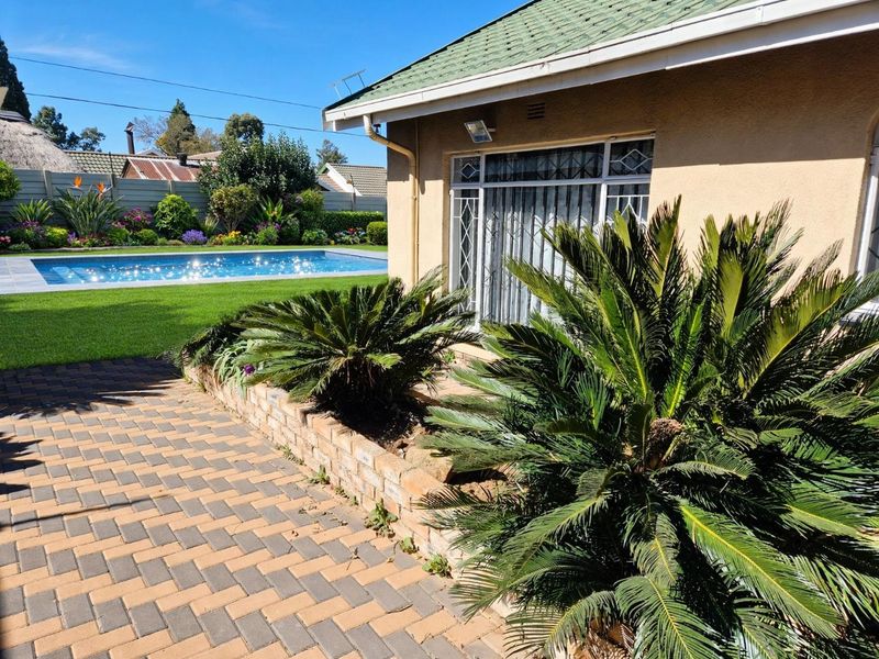 Rear exterior view featuring a well-maintained swimming pool, paved patio area, and established garden landscaping adjacent to the house.