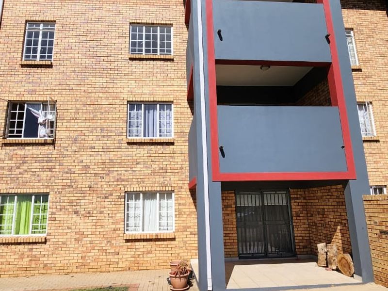 Rear view of a multi-story apartment building featuring brick facade, stacked balconies, and a ground-level paved patio area with lawn.