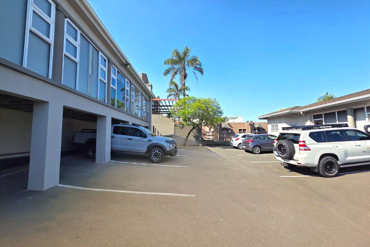 Exterior view of the property featuring a paved parking area with covered bays and multi-pane windows along the building facade.