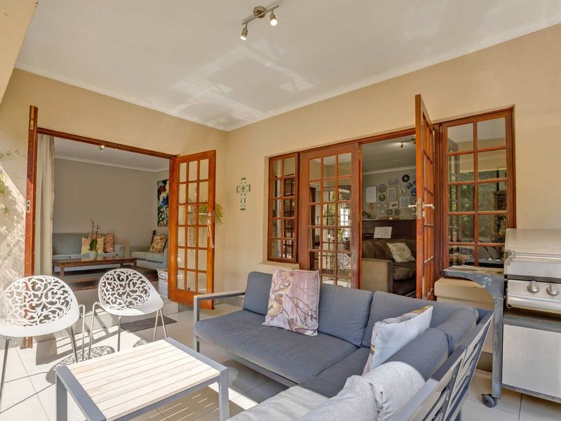 A covered patio area featuring tiled flooring, timber-framed glass doors providing access to the interior, and a built-in gas braai for outdoor entertaining.