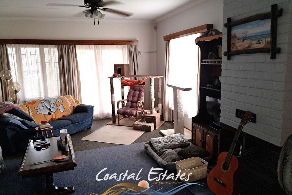 Spacious living room featuring a painted brick fireplace, ceiling fan, and large windows allowing for ample natural light.