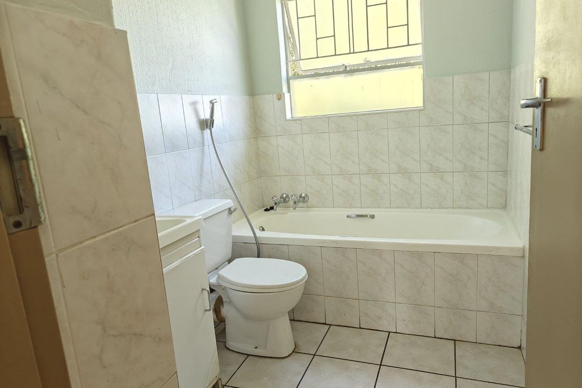 A functional bathroom featuring a built-in bathtub, toilet, and vanity cabinet with tiled walls and flooring, providing a clean and practical space.