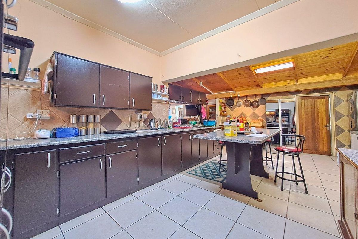 Spacious kitchen featuring dark cabinetry, granite-look countertops, tiled flooring, and a breakfast bar, with a wood-paneled ceiling section in the adjacent area.