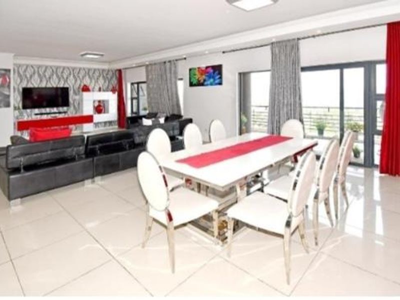 Spacious open-plan living and dining area featuring large format floor tiles, modern recessed lighting, and sliding glass doors leading to an outdoor balcony.