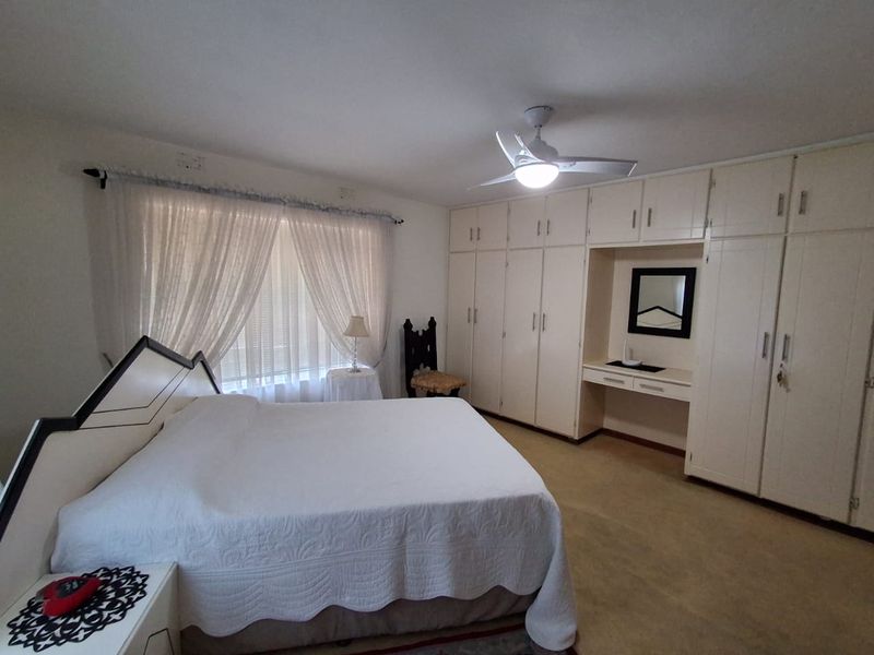 Spacious bedroom featuring extensive built-in cabinetry, a dedicated vanity area, and a ceiling fan, offering a functional layout with neutral finishes.