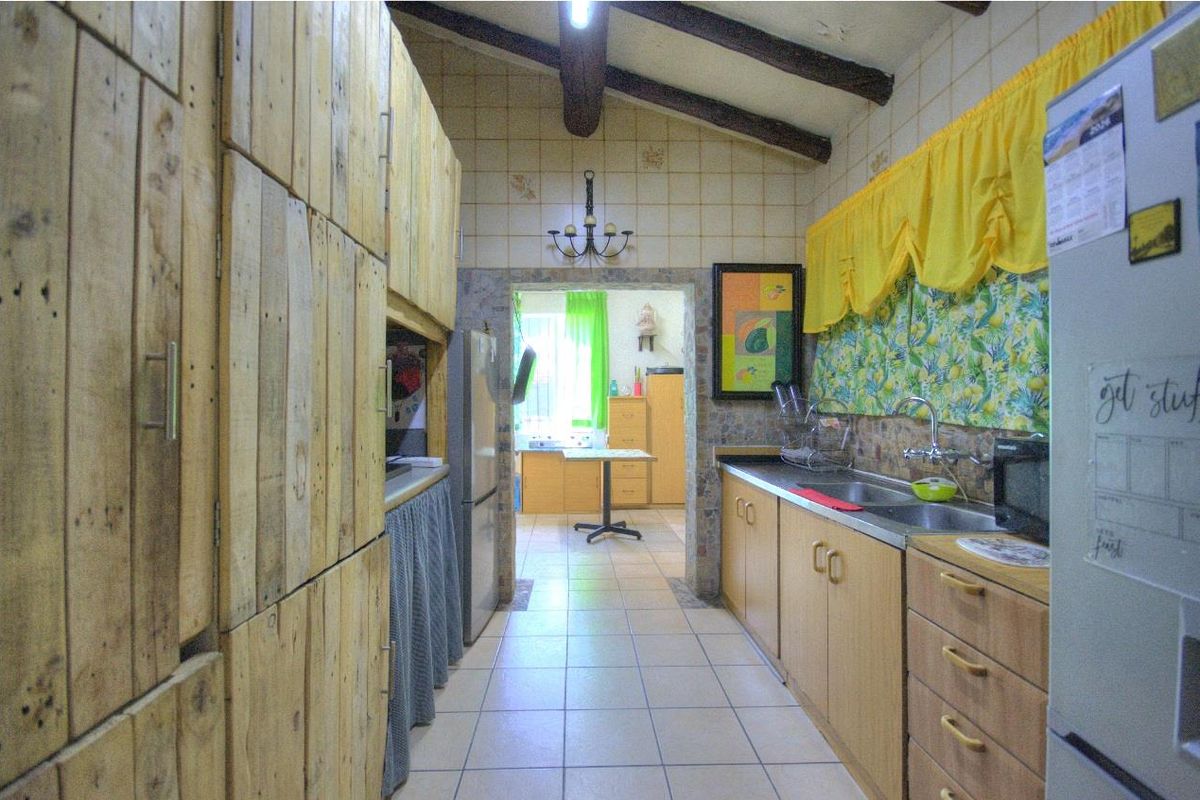A galley-style kitchen featuring wooden cabinetry, tiled splashbacks, and exposed ceiling beams, leading through to an adjacent utility or secondary kitchen area.