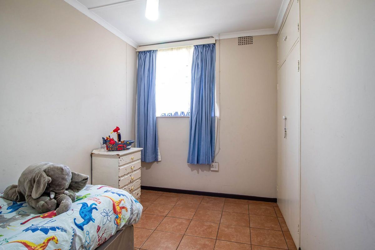 A functional bedroom featuring tiled flooring, built-in cupboards, and a window providing natural light.