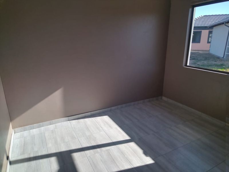 A bright, empty bedroom featuring modern light-toned tiled flooring and a large window with an exterior view.