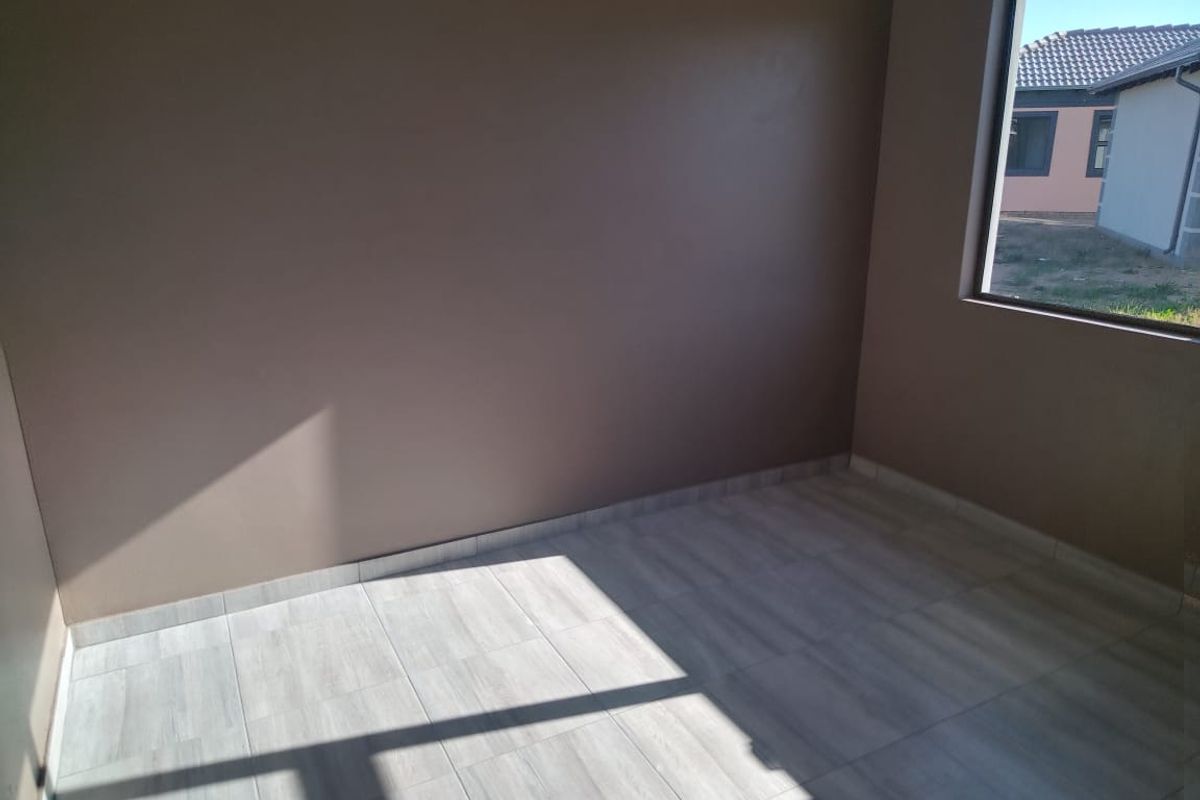 A bright, empty bedroom featuring modern light-toned tiled flooring and a large window with an exterior view.