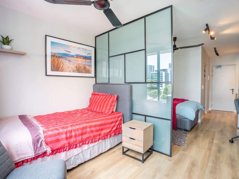 Modern bedroom featuring a stylish frosted glass room divider, ceiling fans, track lighting, and light-toned laminate flooring with a view of the city.