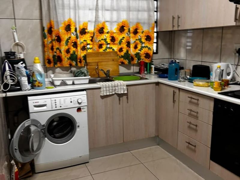A functional kitchen featuring laminate cabinetry, tiled walls and flooring, a built-in oven, and an integrated washing machine space.