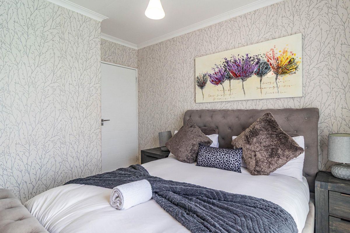A well-maintained bedroom featuring patterned wallpaper, a neutral color palette, and a classic interior door.