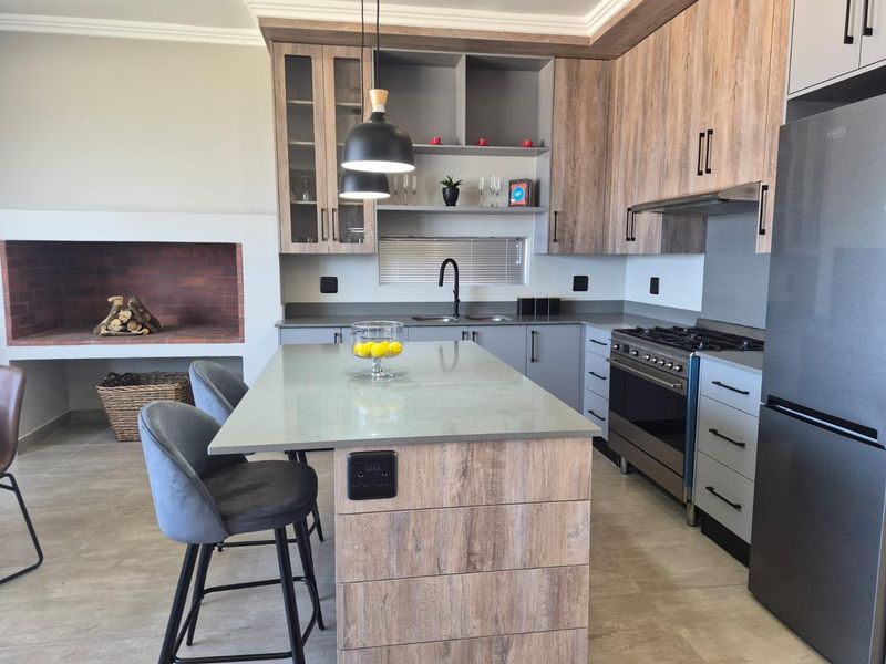 Modern open-plan kitchen featuring wood-finish cabinetry, stone countertops, a central island, gas stove, and an integrated brick fireplace.