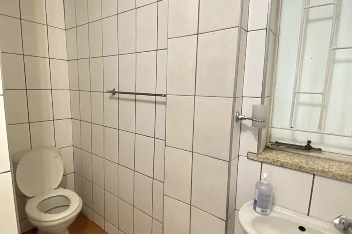 A functional bathroom featuring a wall-mounted basin, toilet, and tiled walls with a wooden ceiling finish.