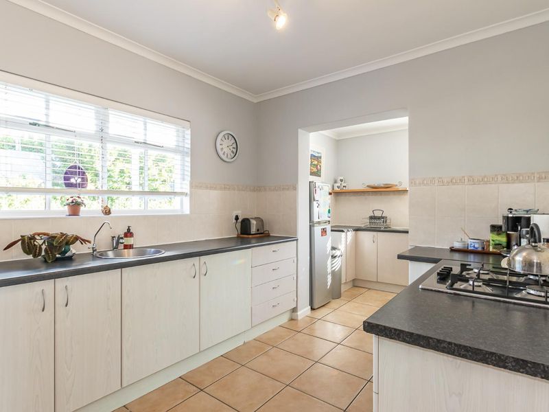 A functional kitchen featuring light-toned cabinetry, dark laminate countertops, a gas hob, and tiled flooring, with an adjoining scullery area.