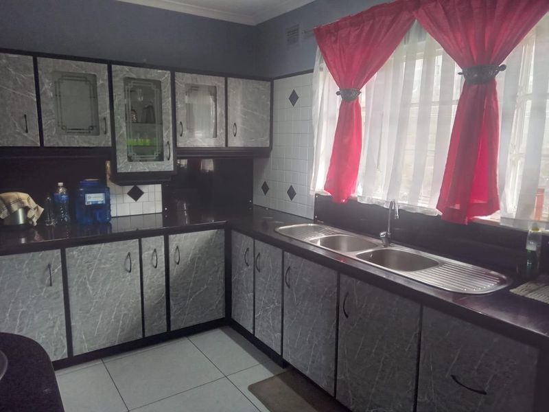 A functional kitchen featuring grey marble-effect cabinetry, a double bowl stainless steel sink, and tiled splashbacks with a window view.