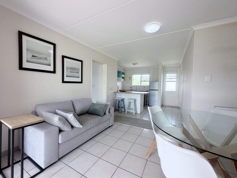 An open-plan living and dining area featuring tiled flooring, a functional kitchen with a breakfast counter, and neutral wall finishes.