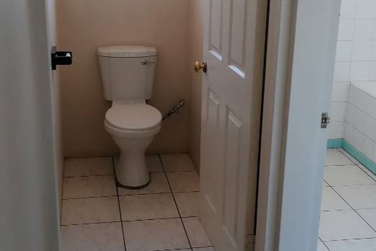 A compact, functional bathroom featuring a toilet, tiled flooring, and a window, adjacent to a hallway with parquet flooring.