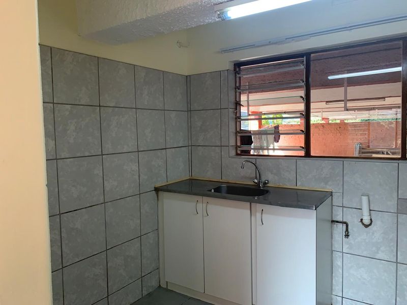 A functional scullery or utility area featuring a stainless steel sink, built-in base cabinetry, and tiled splashback, providing a practical space for wash-up tasks.