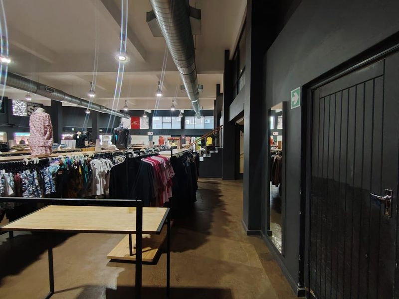 Spacious retail interior featuring industrial-style exposed ducting, polished concrete flooring, and a modern dark color palette with integrated staircase access.