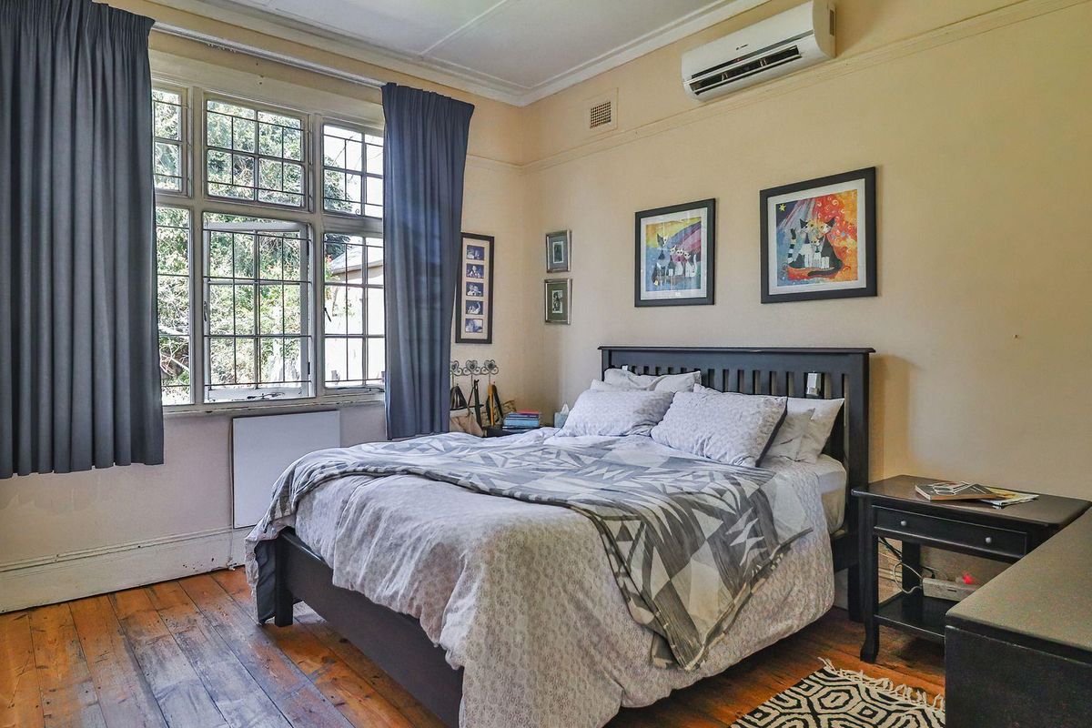 A well-proportioned bedroom featuring original timber flooring, classic leaded glass windows, and a wall-mounted split system air conditioner for climate control.