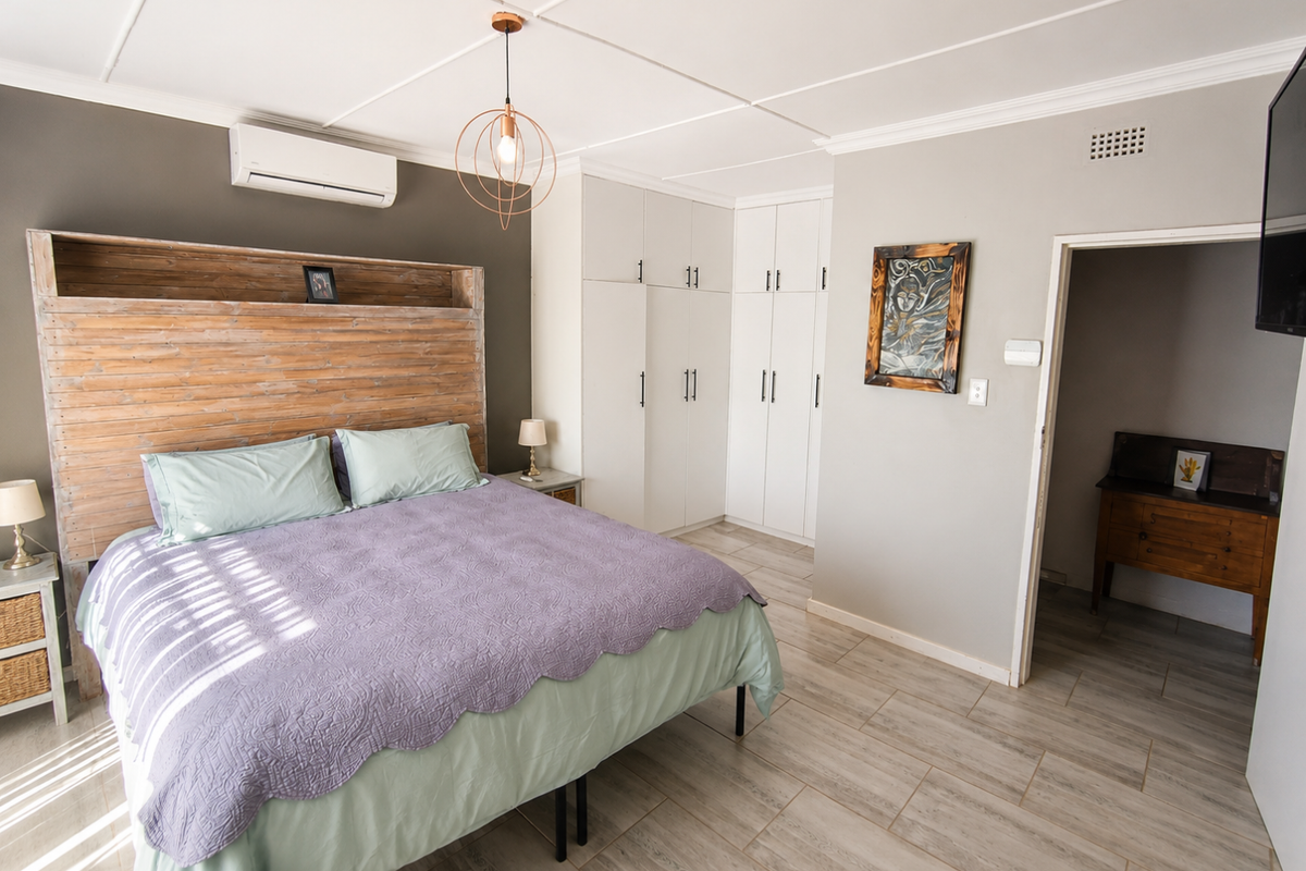 A well-maintained bedroom featuring built-in floor-to-ceiling wardrobes, tiled flooring, and a wall-mounted air conditioning unit.