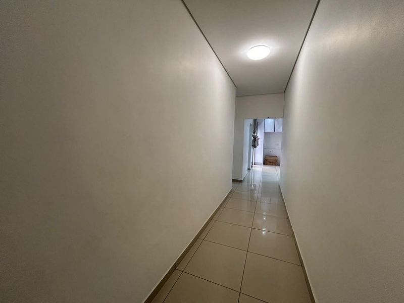 A clean, minimalist hallway featuring neutral tiled flooring and recessed ceiling lighting, providing a bright transition space between rooms.