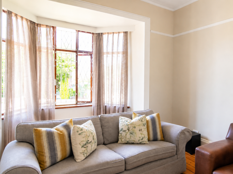A bright living room featuring a classic bay window with leaded glass, original timber window frames, and polished timber flooring.
