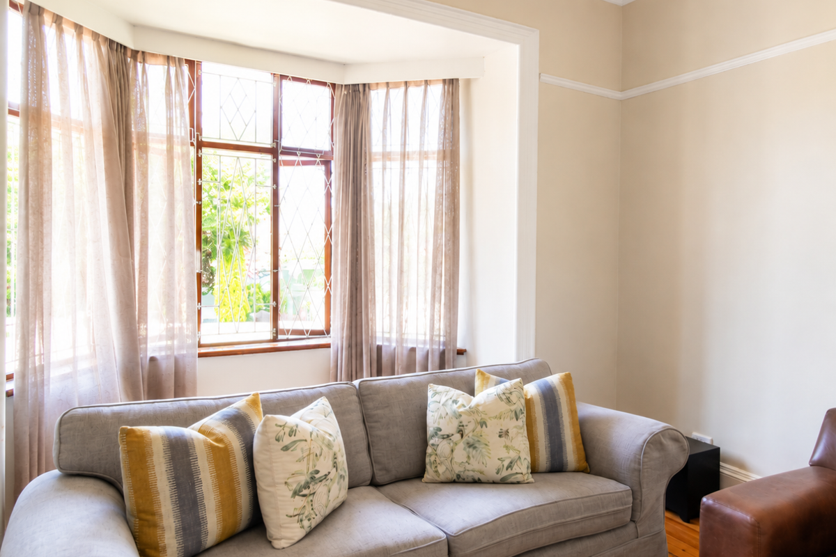 A bright living room featuring a classic bay window with leaded glass, original timber window frames, and polished timber flooring.