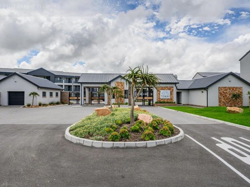 Front entrance view of the apartment complex featuring a paved driveway, landscaped traffic island, and modern stone-clad building facade.