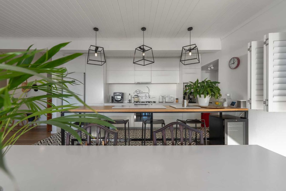 Modern kitchen featuring sleek white cabinetry, a warm wooden breakfast bar, integrated appliances, and stylish pendant lighting under a classic tongue and groove ceiling.