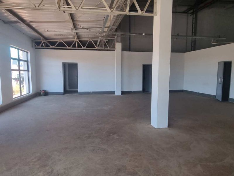 Spacious open-plan industrial unit featuring exposed steel roof trusses, large windows for natural light, and durable concrete flooring.