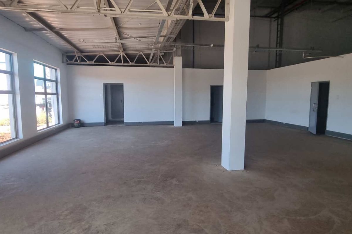 Spacious open-plan industrial unit featuring exposed steel roof trusses, large windows for natural light, and durable concrete flooring.