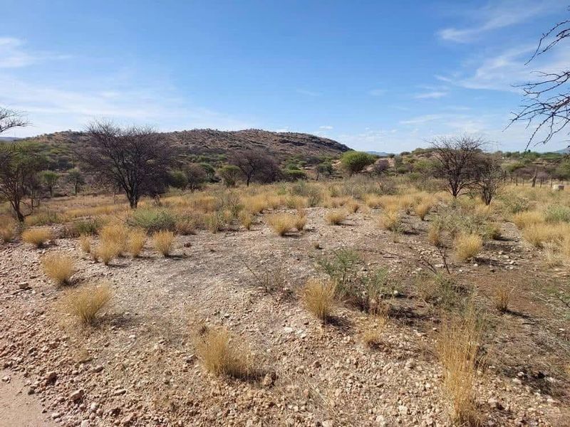 A wide-angle view of the vacant residential land featuring natural rocky terrain, indigenous vegetation, and scenic mountain views in the distance.