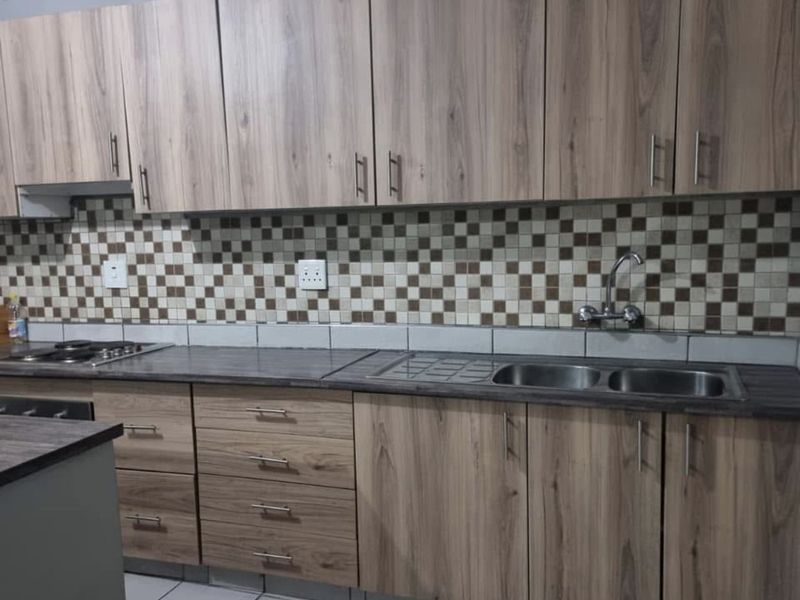A functional kitchen featuring wood-look laminate cabinetry, a mosaic tile backsplash, double stainless steel sink, and built-in hob with ample counter space.