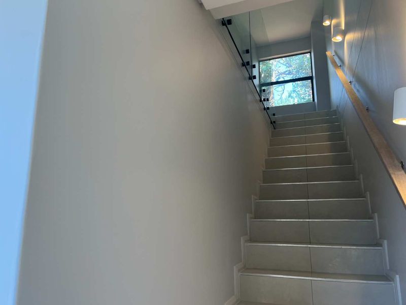 Modern staircase featuring tiled steps, a sleek glass balustrade with a timber handrail, and integrated wall lighting.