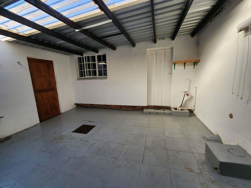 A functional laundry area featuring tiled flooring, plumbing connections, and a covered roof structure, providing a practical space for utility needs.