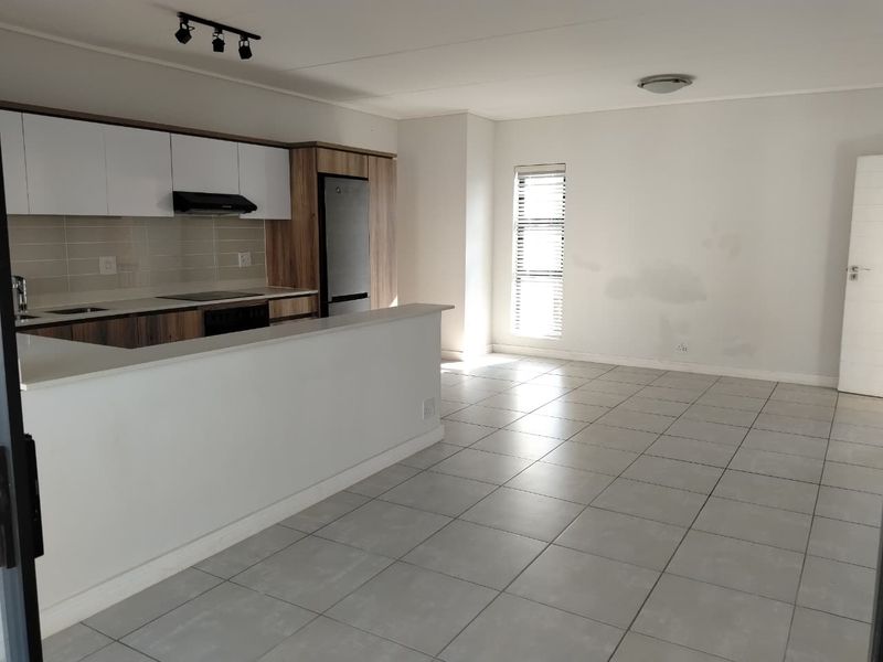 Open-plan living and kitchen area featuring modern cabinetry, tiled flooring, and a breakfast bar, offering a clean, versatile space ready for personalization.