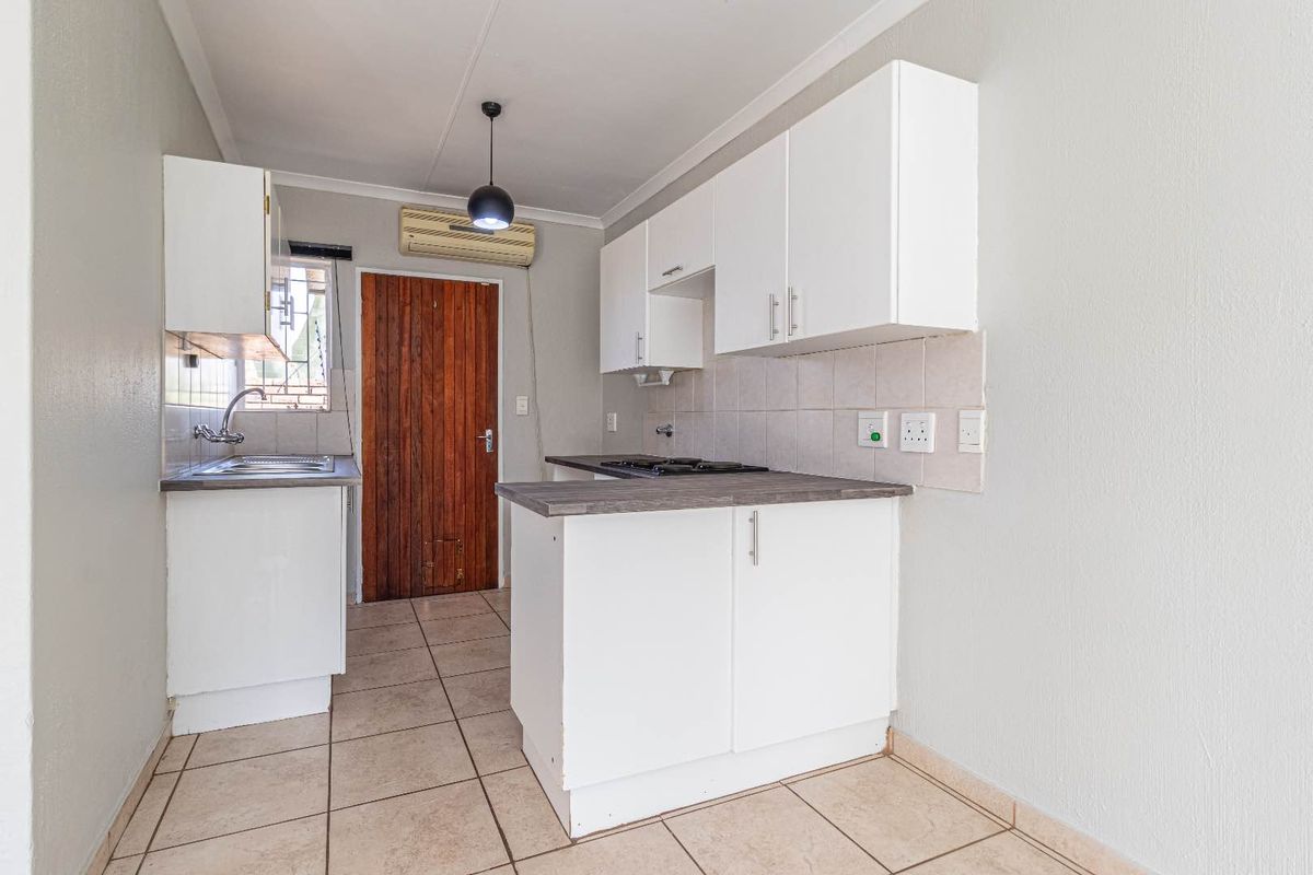 A functional kitchen featuring white cabinetry, dark laminate countertops, a built-in hob, and tiled flooring with direct access to an exterior door.
