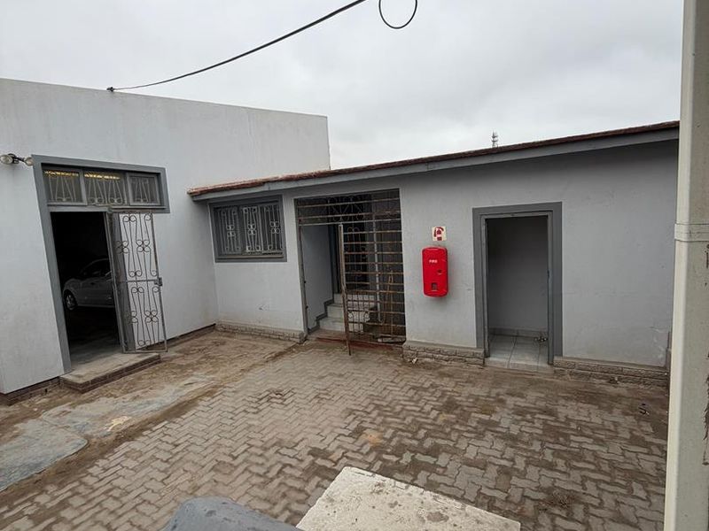 A paved rear courtyard area featuring multiple access points with security gates and a wall-mounted fire extinguisher.