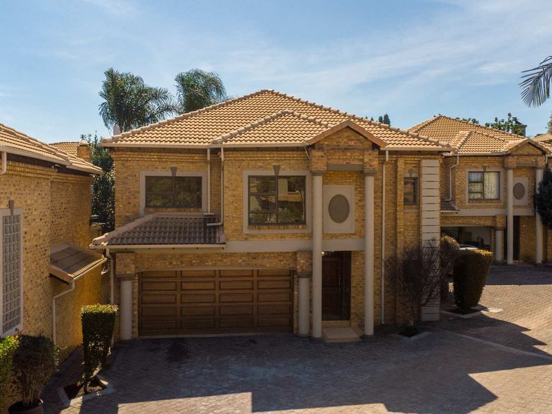 Front elevation of a double-storey face brick townhouse featuring a tiled roof, decorative columns, and a paved driveway with integrated double garage.