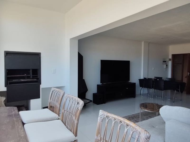 Open plan living area featuring tiled floors and a built-in braai, seamlessly connecting the indoor space with a bright, window-lined sunroom or balcony area.