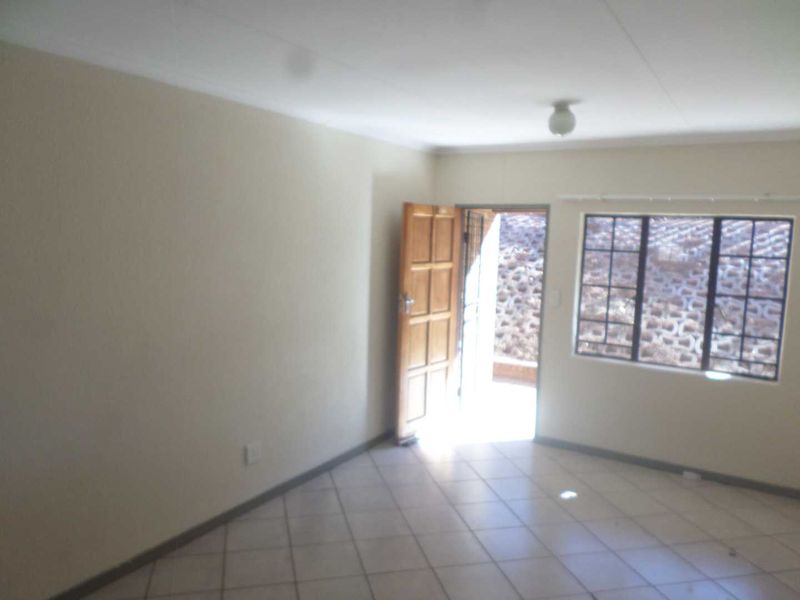 An empty living room featuring tiled flooring, a wooden entrance door, and windows fitted with security burglar bars.