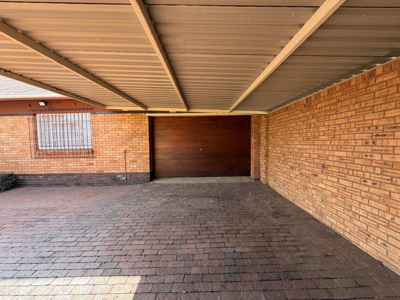 A covered carport area featuring brick paving, facebrick walls, and a secure sectional garage door.